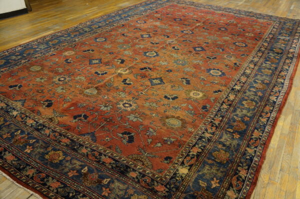Large rusty red rug with an all-over floral pattern and a wide navy and blue border on wood floors.