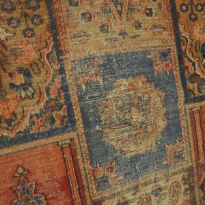 Heavily distressed patchwork rug closeup featuring traditional motifs in faded blue, rust, and tan colors.
