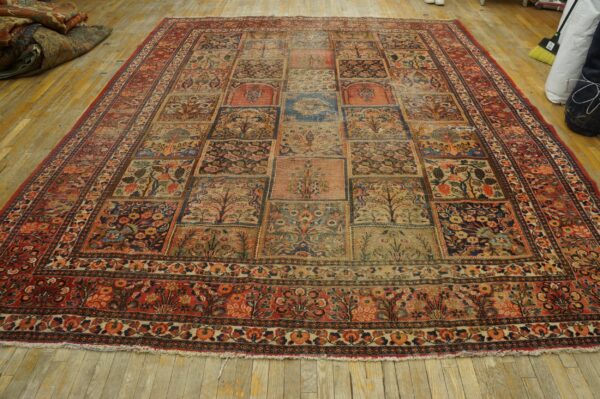 Muted rectangular rug with a complex, grid-like pattern featuring floral and tree motifs on distressed wood flooring.