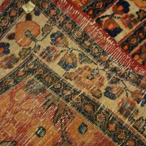 Detailed view of a rug corner with traditional motifs in orange, red, navy, and tan colors.