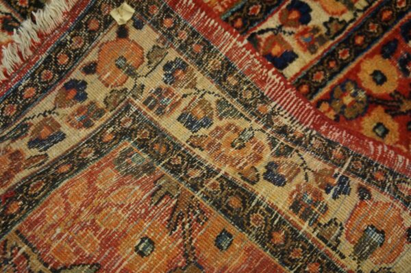 Detailed view of a rug corner with traditional motifs in orange, red, navy, and tan colors.