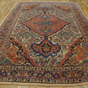 Intricate patterned rug in deep blue and terracotta against a cream background, displayed on worn hardwood.