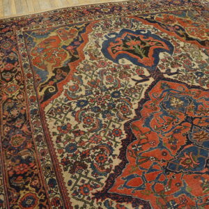Rust and blue traditional patterned rug with a beige field, laid on light wooden plank floors.