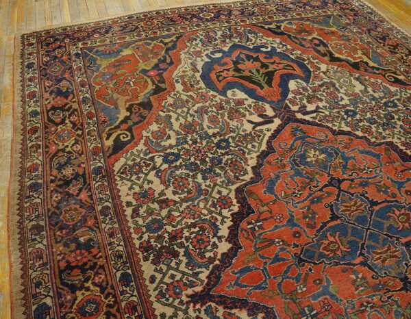 Rust and blue traditional patterned rug with a beige field, laid on light wooden plank floors.