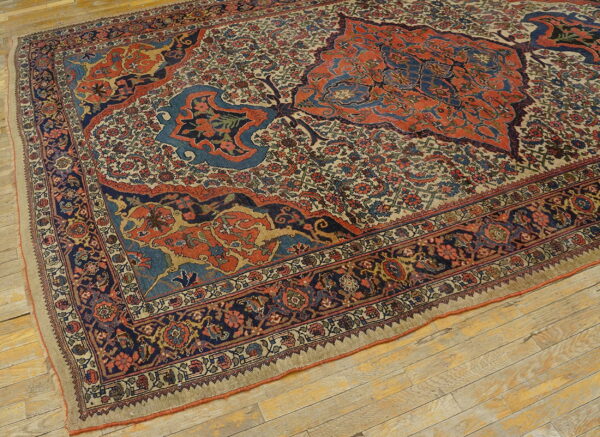 Blue and orange traditional rug with an intricate floral field sits on distressed light wood floors.