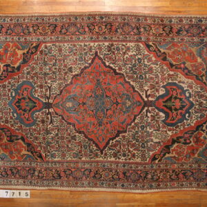 Ornate red and blue medallion rug on a cream ground, displayed flat on light wood planks.