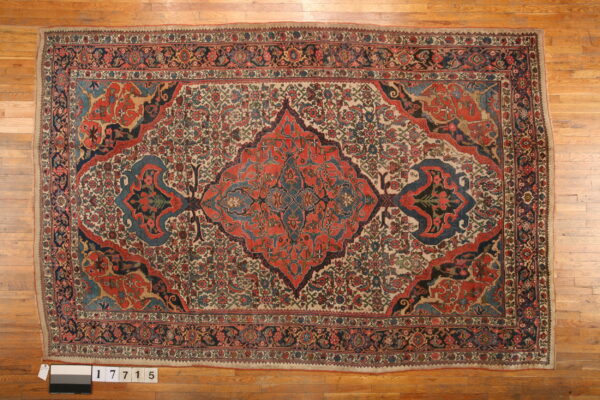 Ornate red and blue medallion rug on a cream ground, displayed flat on light wood planks.