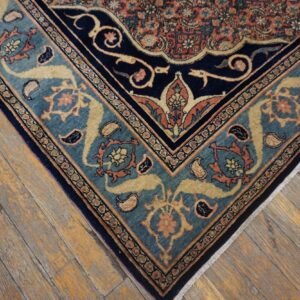 Detail of a traditional patterned rug with navy, teal, and orange borders on rustic hardwood flooring.