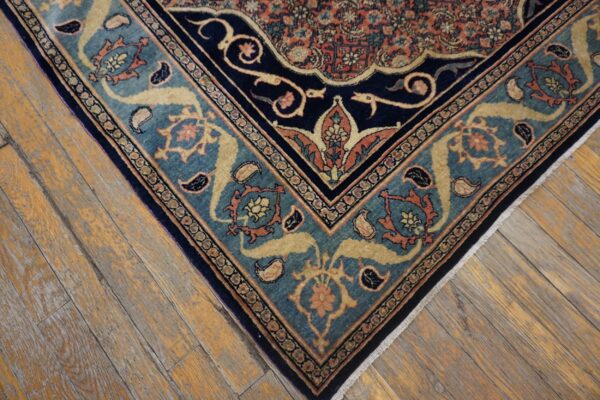 Detail of a traditional patterned rug with navy, teal, and orange borders on rustic hardwood flooring.