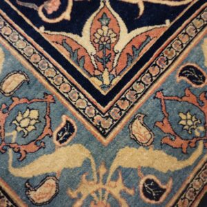Detailed view of a navy and teal rug featuring gold and orange floral patterns on wood flooring.
