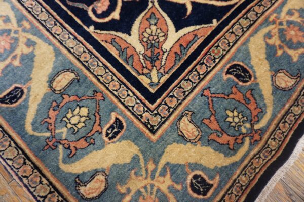 Detailed view of a navy and teal rug featuring gold and orange floral patterns on wood flooring.