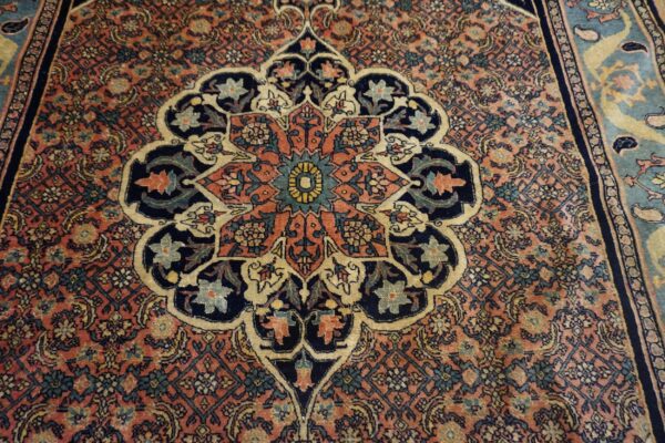 Close-up of an ornate rug featuring a central medallion in navy, coral, cream, and teal colors.