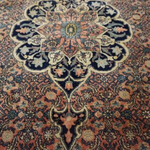 Intricate traditional rug pattern featuring navy and teal designs set against a dusty pink background field.