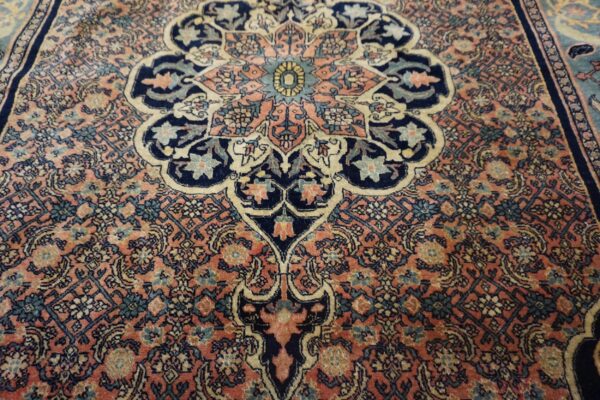 Intricate traditional rug pattern featuring navy and teal designs set against a dusty pink background field.