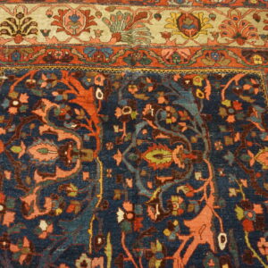 Ornate traditional rug with a navy blue field, coral and green floral motifs, and a wide light beige border.