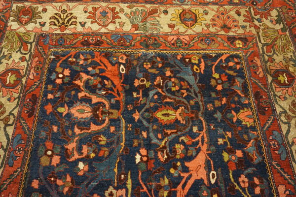 Ornate traditional rug with a navy blue field, coral and green floral motifs, and a wide light beige border.