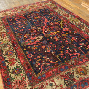 Ornate rug featuring a deep blue field and a complex red and tan floral border on light wood flooring.