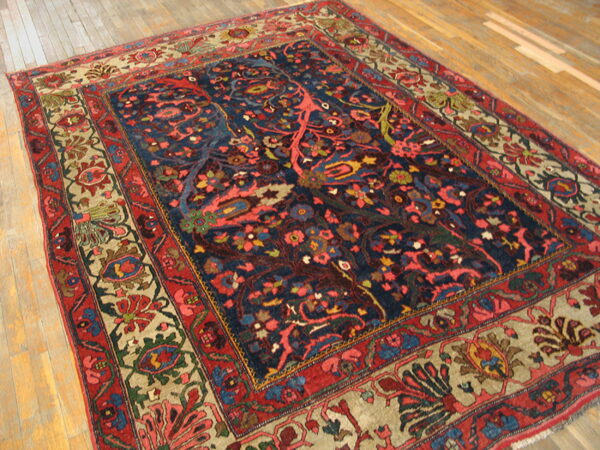 Ornate rug featuring a deep blue field and a complex red and tan floral border on light wood flooring.