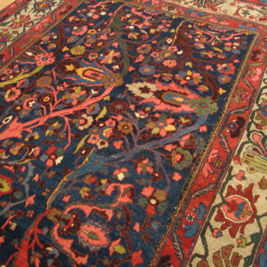 Traditional navy rug with dense coral, red, and green floral patterns rests on wood floorboards.