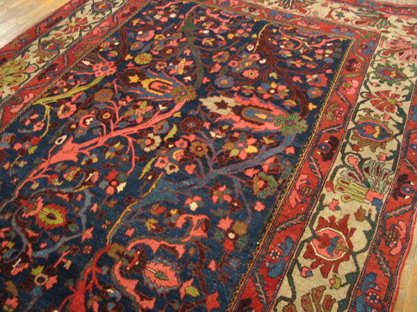 Traditional navy rug with dense coral, red, and green floral patterns rests on wood floorboards.