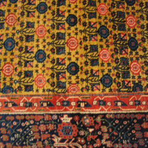 Rug detail showing yellow field with blue and red motifs bordered by a red band and dense dark navy pattern.