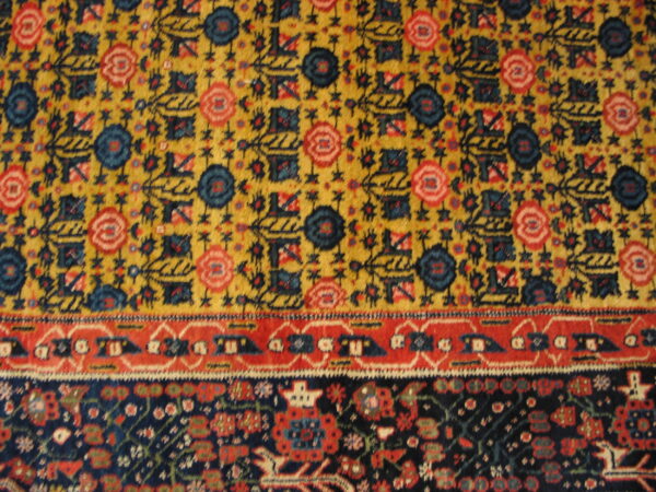 Rug detail showing yellow field with blue and red motifs bordered by a red band and dense dark navy pattern.