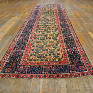 Narrow runner rug with a gold field and navy borders rests on light-colored plank flooring.