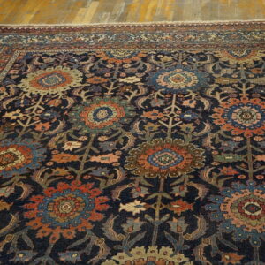 Dark blue rug featuring a complex traditional pattern of orange, blue, and cream floral medallions on wood flooring.
