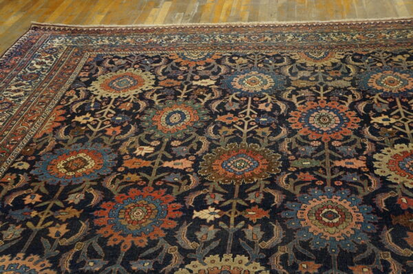 Dark blue rug featuring a complex traditional pattern of orange, blue, and cream floral medallions on wood flooring.
