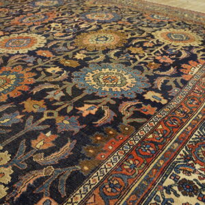 Intricate navy blue rug with dense floral patterns in rust, gold, and light blue on wood flooring.