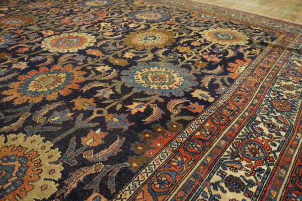 Intricate navy blue rug with dense floral patterns in rust, gold, and light blue on wood flooring.