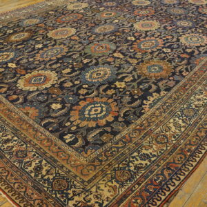 Muted floral rug in dark blue, rust, and gold on a distressed wooden plank floor.