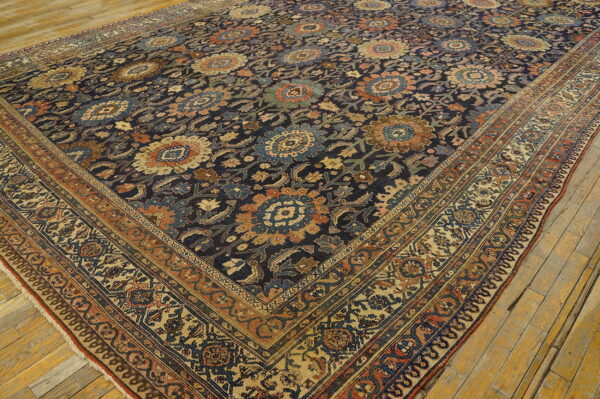 Muted floral rug in dark blue, rust, and gold on a distressed wooden plank floor.