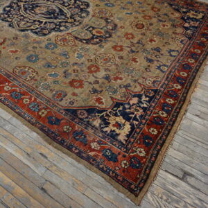 Distressed khaki rug with navy and red floral patterns lies on light gray weathered wooden floorboards.