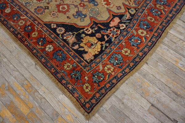 Low pile rug corner shows red and navy floral borders meeting a tan field on weathered wood planks.
