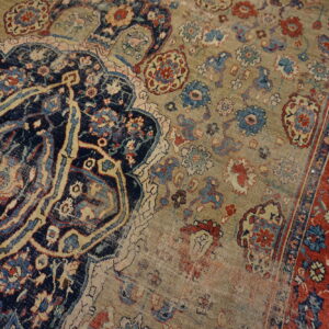 Worn traditional area rug featuring a navy center design, red border, and beige field with floral motifs.