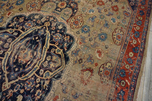 Worn traditional area rug featuring a navy center design, red border, and beige field with floral motifs.