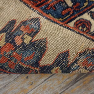 Traditional blue and red patterned rug is curled, exposing the light brown woven backing on wood flooring.