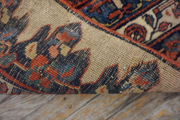Traditional blue and red patterned rug is curled, exposing the light brown woven backing on wood flooring.