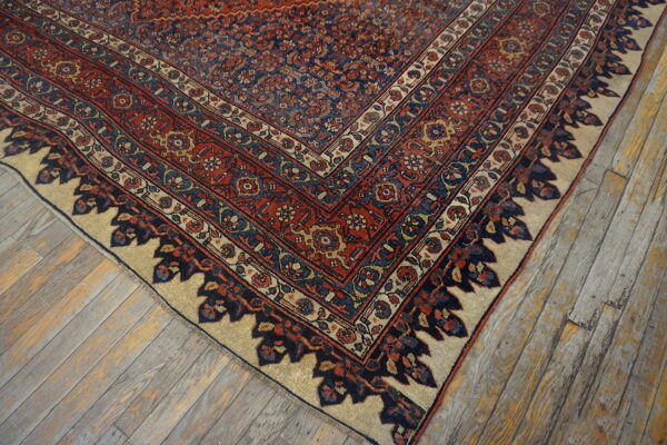 Ornate navy and red patterned rug with a wide beige border lies on rustic, gray wooden floorboards.