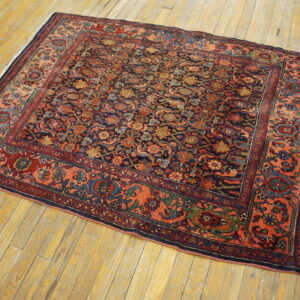 Ornate navy and red floral rug with a wide coral border rests on worn yellow wood floors.