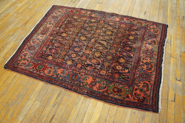 Ornate navy and red floral rug with a wide coral border rests on worn yellow wood floors.