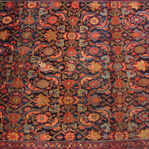 Dark blue rug features a dense traditional pattern accented with rust red, teal, and olive motifs.
