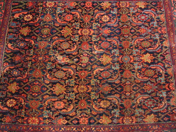 Dark blue rug features a dense traditional pattern accented with rust red, teal, and olive motifs.