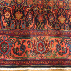 Detailed view of the rug's navy field and coral border with complex floral medallion patterns.