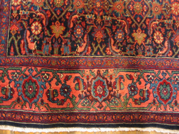 Detailed view of the rug's navy field and coral border with complex floral medallion patterns.