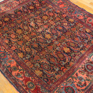 Intricate navy and coral rug with dense floral motifs rests on light wood plank flooring.