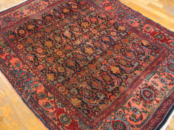 Intricate navy and coral rug with dense floral motifs rests on light wood plank flooring.