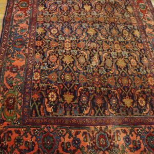 Ornate navy and coral rug with complex floral designs sits on light hardwood plank flooring.