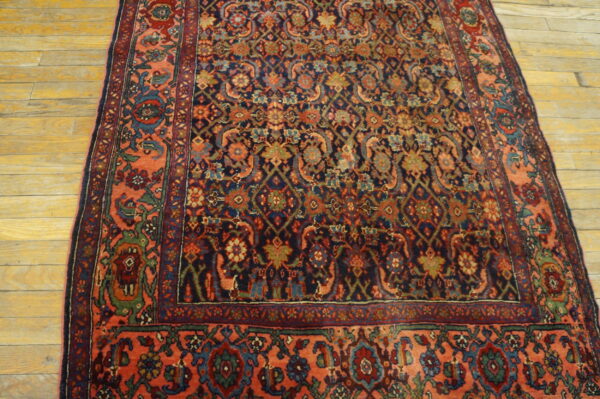 Ornate navy and coral rug with complex floral designs sits on light hardwood plank flooring.